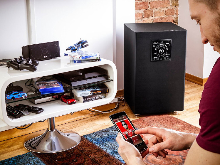 Subwoofer des 5.1-Sets Concept E mit jungem Mann mit Smartphone in der Hand.