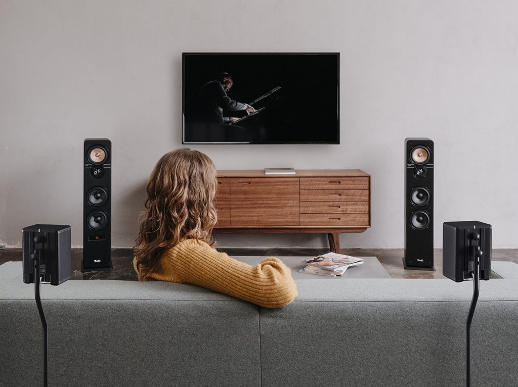 A woman watches TV with a surround-sound setup from Teufel