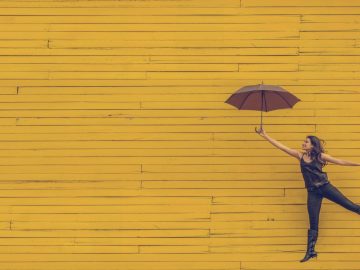 woman holding umbrella jumping against a yellow wooden backdrop