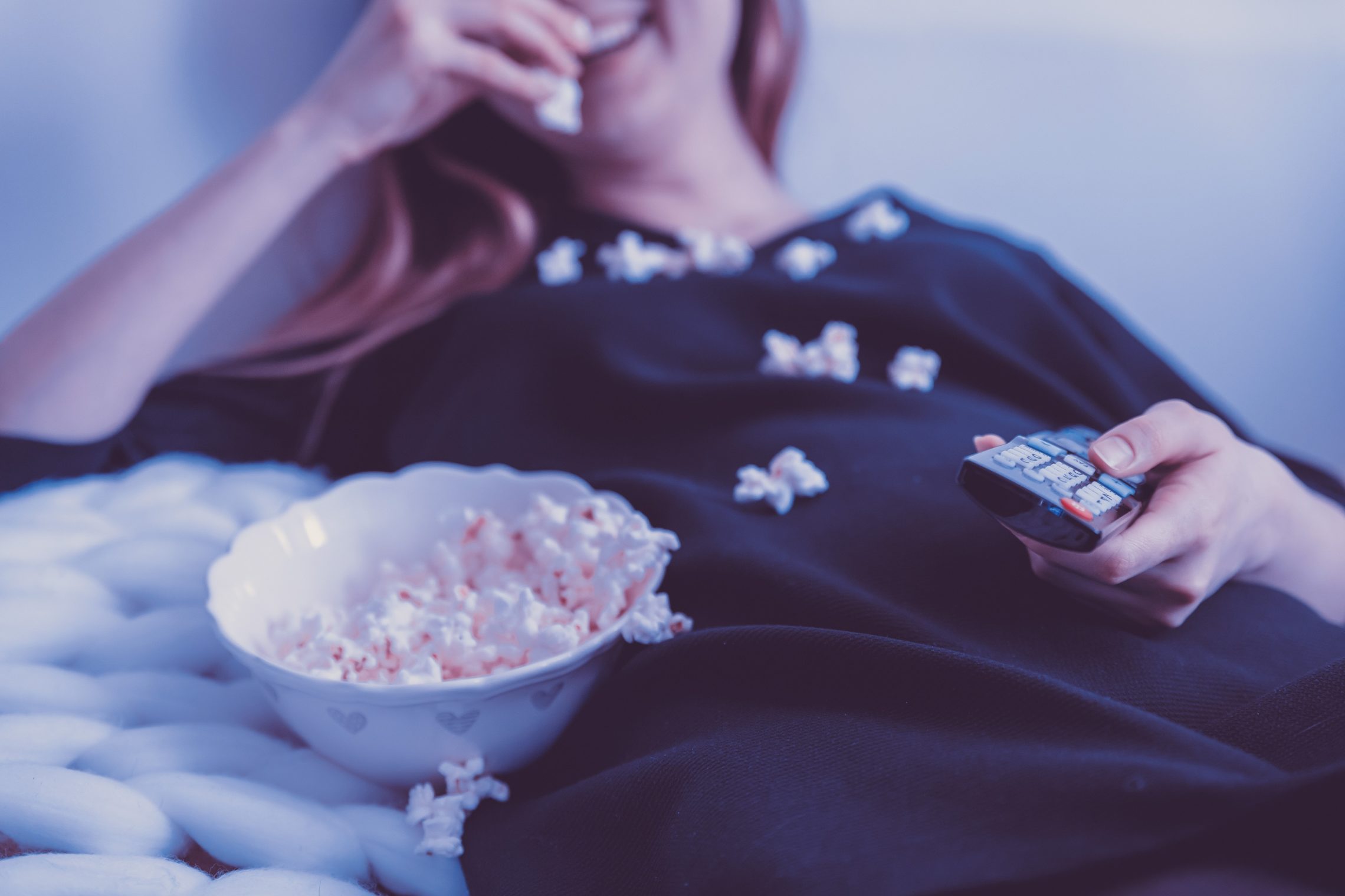 Woman is watching TV and eating popcorn.