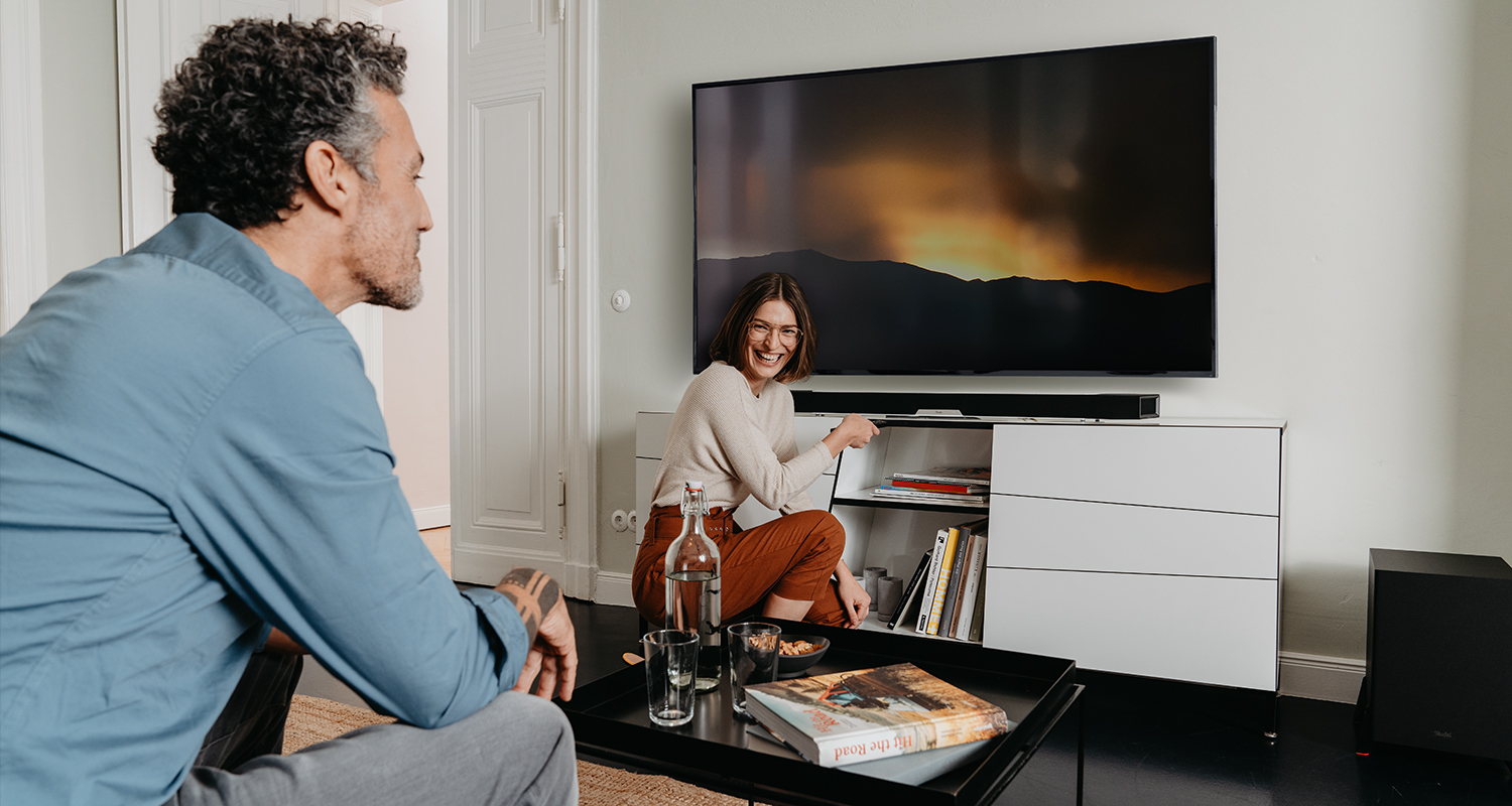 Mann auf Sofa und Frau vor Soundbar und Fernseher