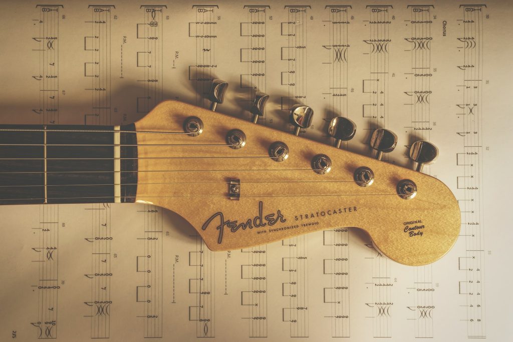 The headstock of a Fender Stratocaster laying on a piece of guitar tablature